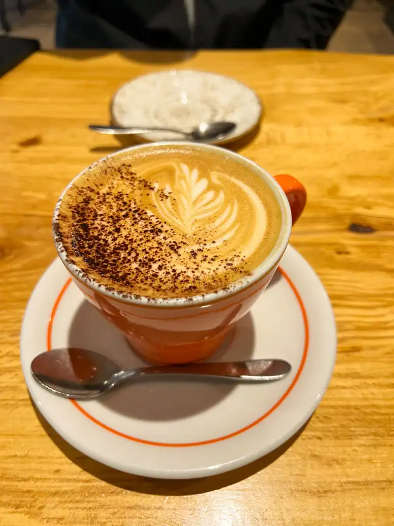 A perfect latte with a spoon, leaf design and cinnamon sprinkled on top. 