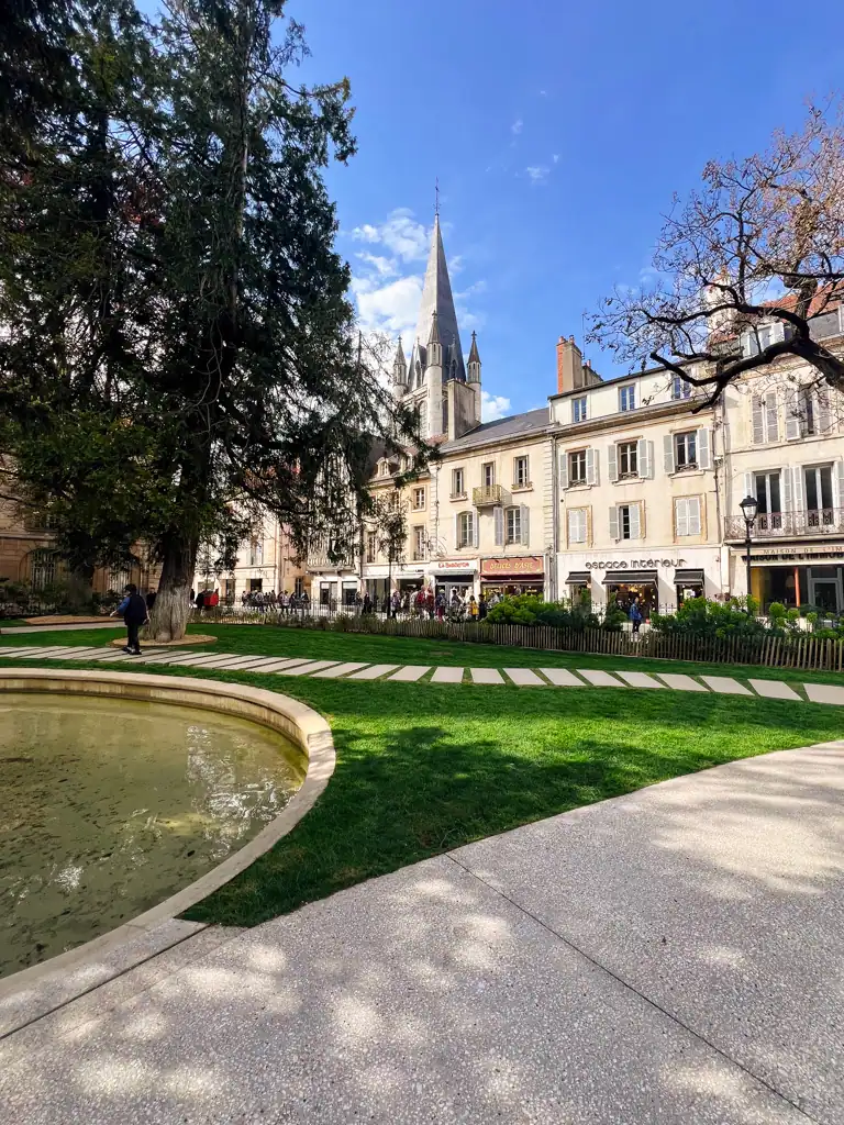 A square in Dijon  with grass, a fountain and large spire in the background on the Dijon Owl Trail