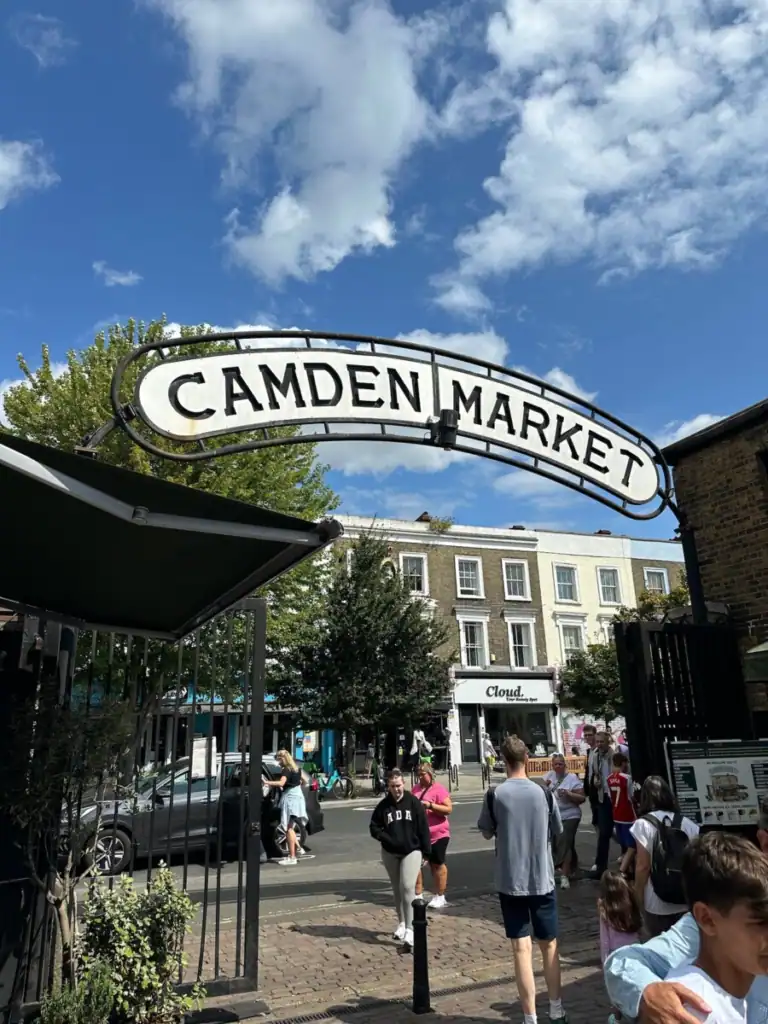 A large sign that says camden market with people walking below the best place to stay in london.