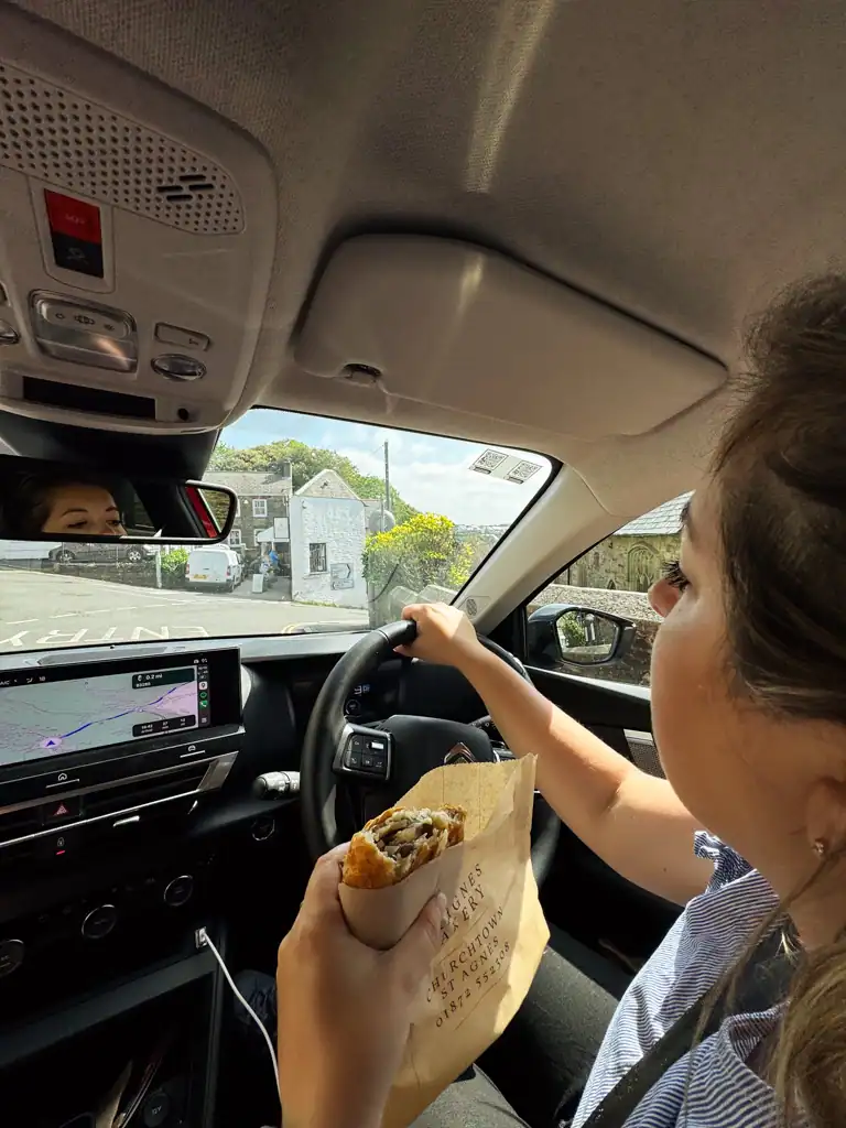 Woman eats Cornish pasty while driving rental car on the left in England. 