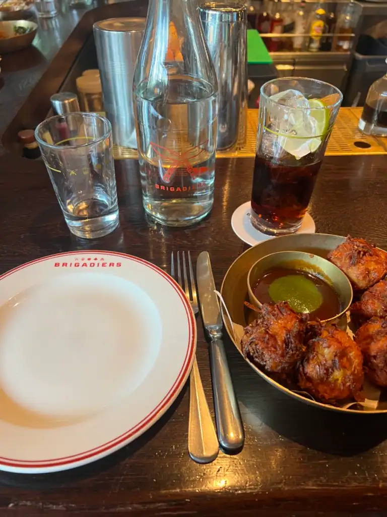 A close up of a place setting at Brigadiers in london. With a plate, glasses and food on the right. 