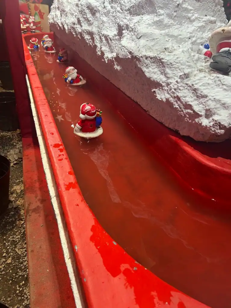 Little santa figurines floating in a red stream with fake snow on the side. 