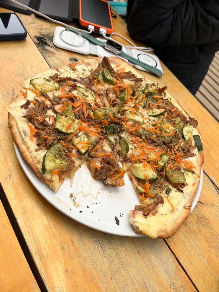 a pizza with zucchini, pork and shredded carrot. 