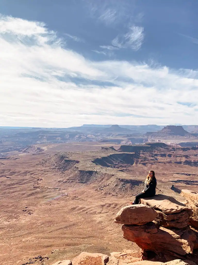 woman sits on rock overlooking canyon lands national park. 