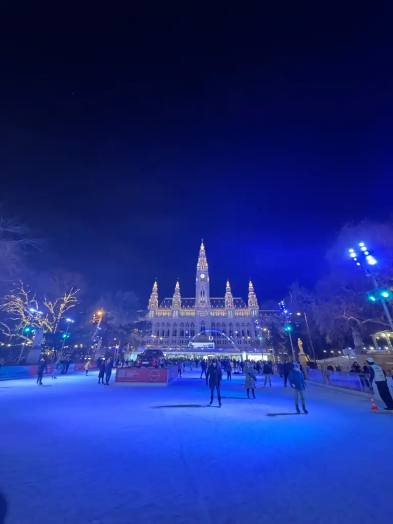 a lit up ice rink with an impressive historical building in the background. 