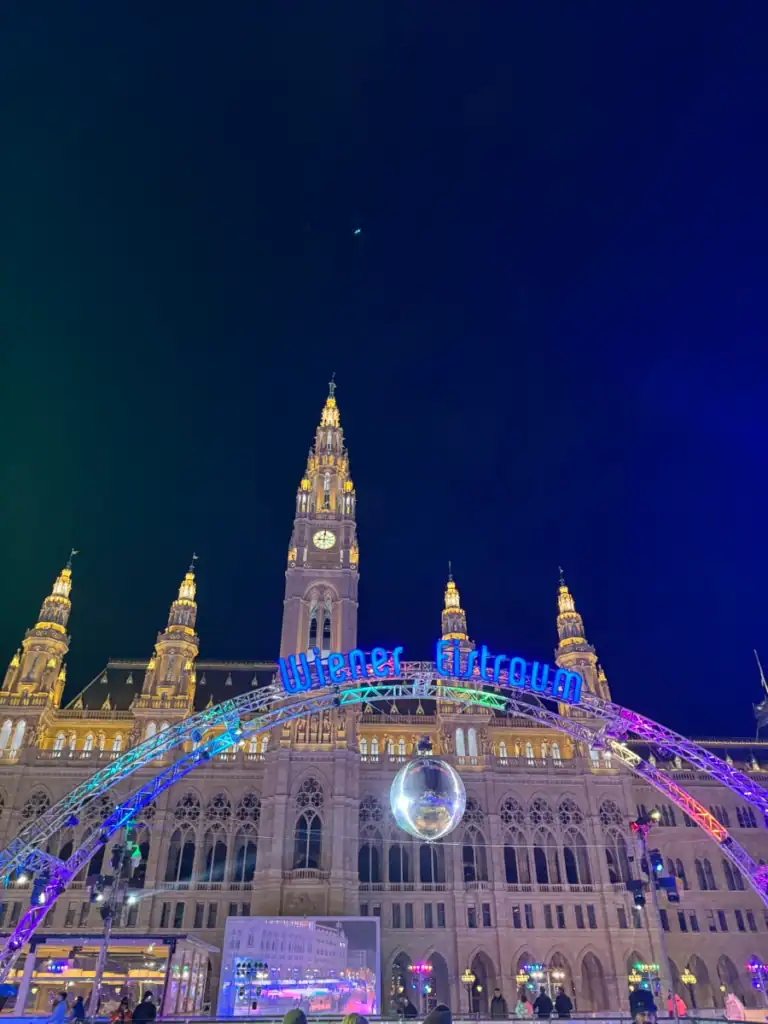 A close up of a lit up building with a neon sign below saying Wiener Eistroum. 