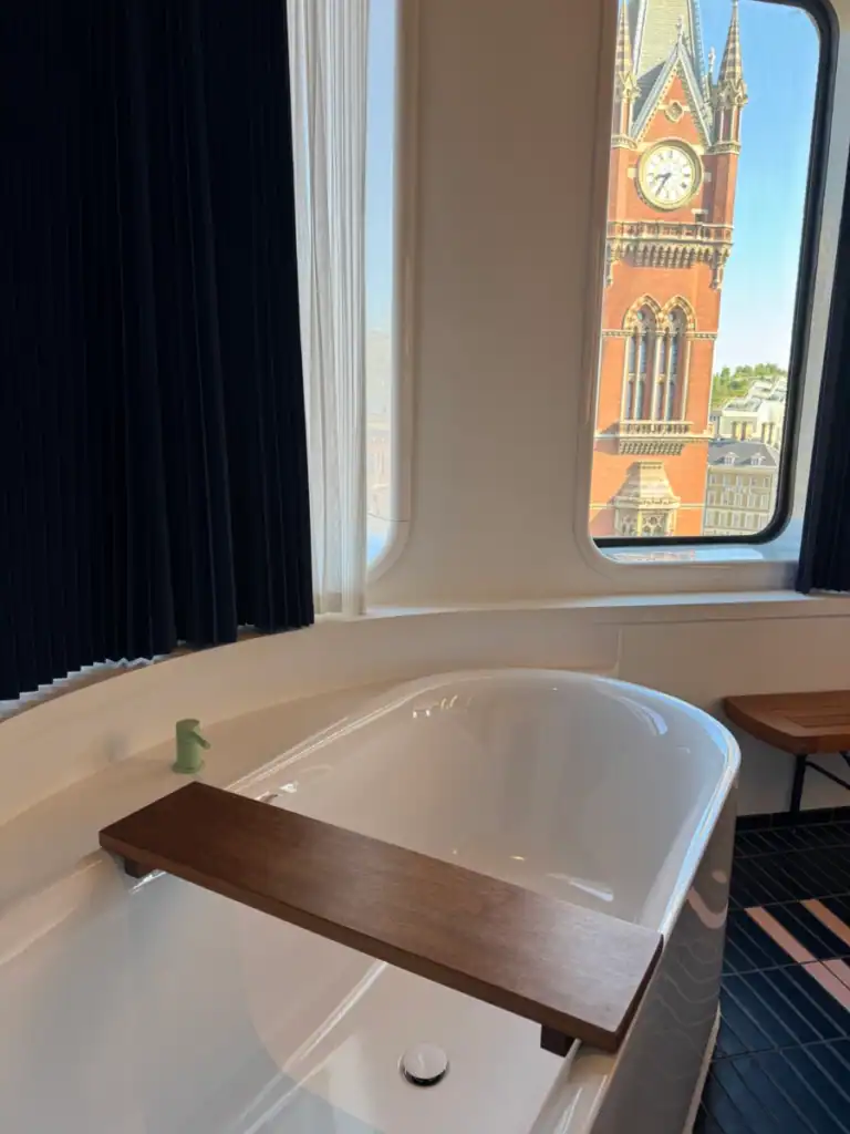 The inside of a hotel room with a large bathtub and st. Pancras out through the window.