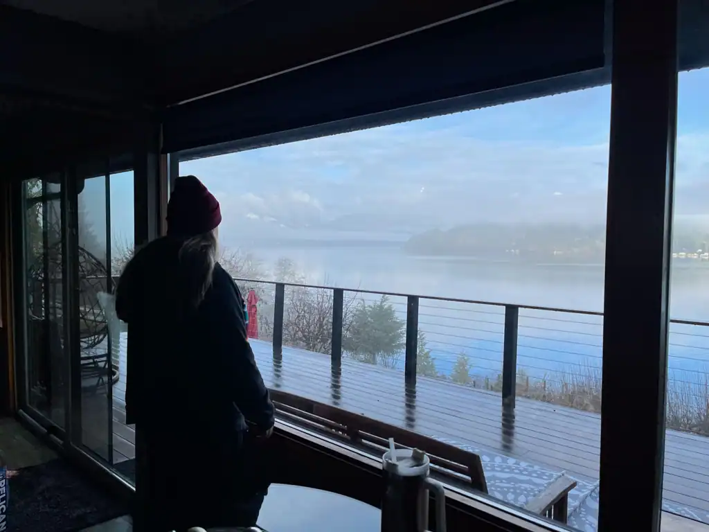 A girl in a red beanie looks outside at a foggy lake at ladies reading weekend. 