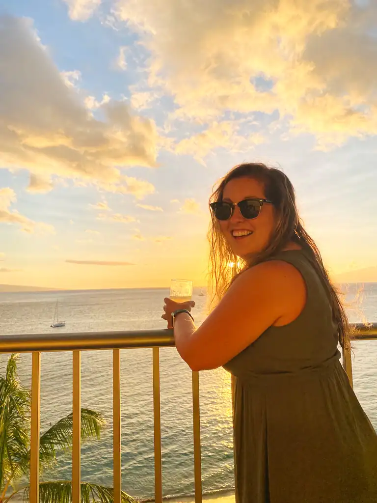 Girl drinks a cocktail on a terrace with the ocean in the background in Maui. 