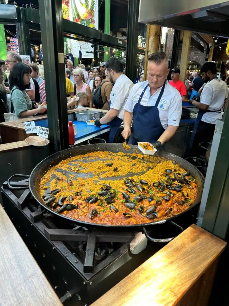 A man stands serving paella from a giant wok at Borough market. 
