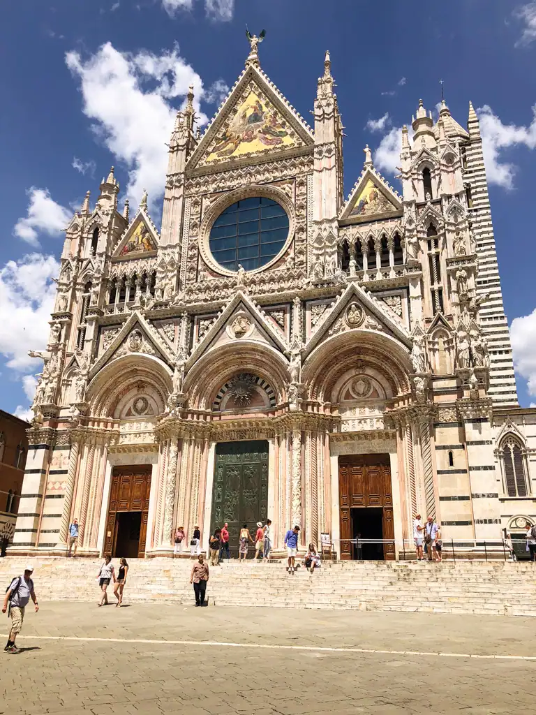 The intricate facade of the Siena Cathedral with small details and a large window in the middle in 5 towns to visit in tuscany. 