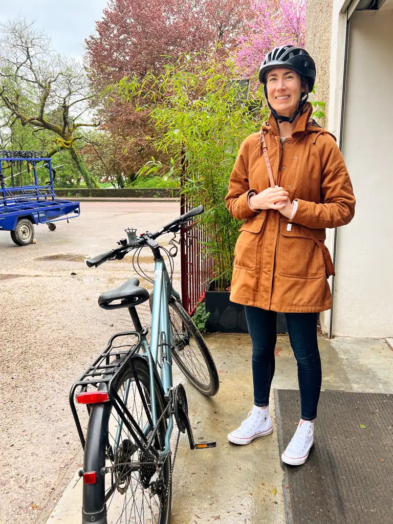 A girl in a brown coat stands by a bike with her helmet on as he readies for the burgundy wine tour. 