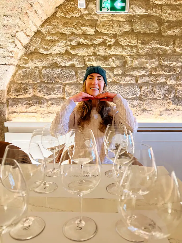 A girl poses in front of many wine glasses. 