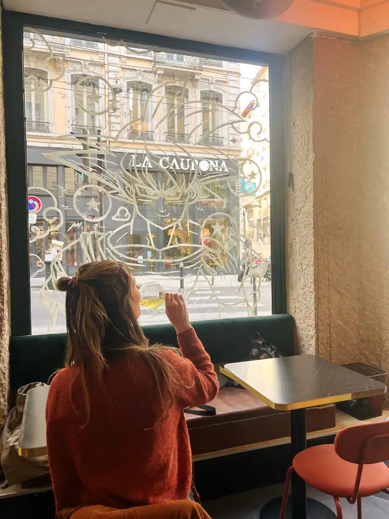 A girl drinks a glass of wine in front of a window with an etching of Goku from Dragon Ball z