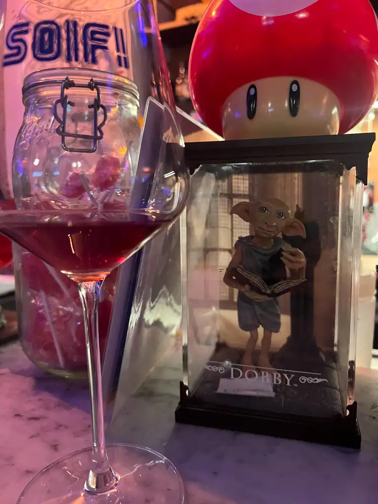 A glass of wine from Soif! one of the best bars in lyon with a nintendo mushroom and dobby statue in the background. 