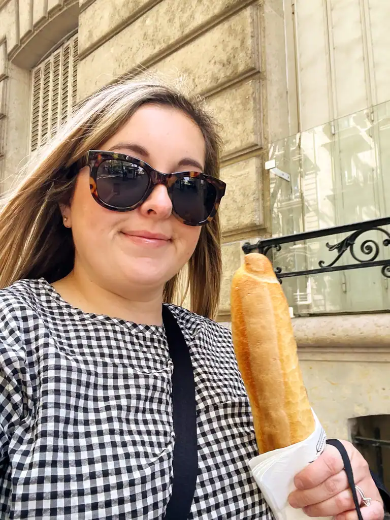 A girl in a black gingham top holding a baguette on a Paris spring day. 