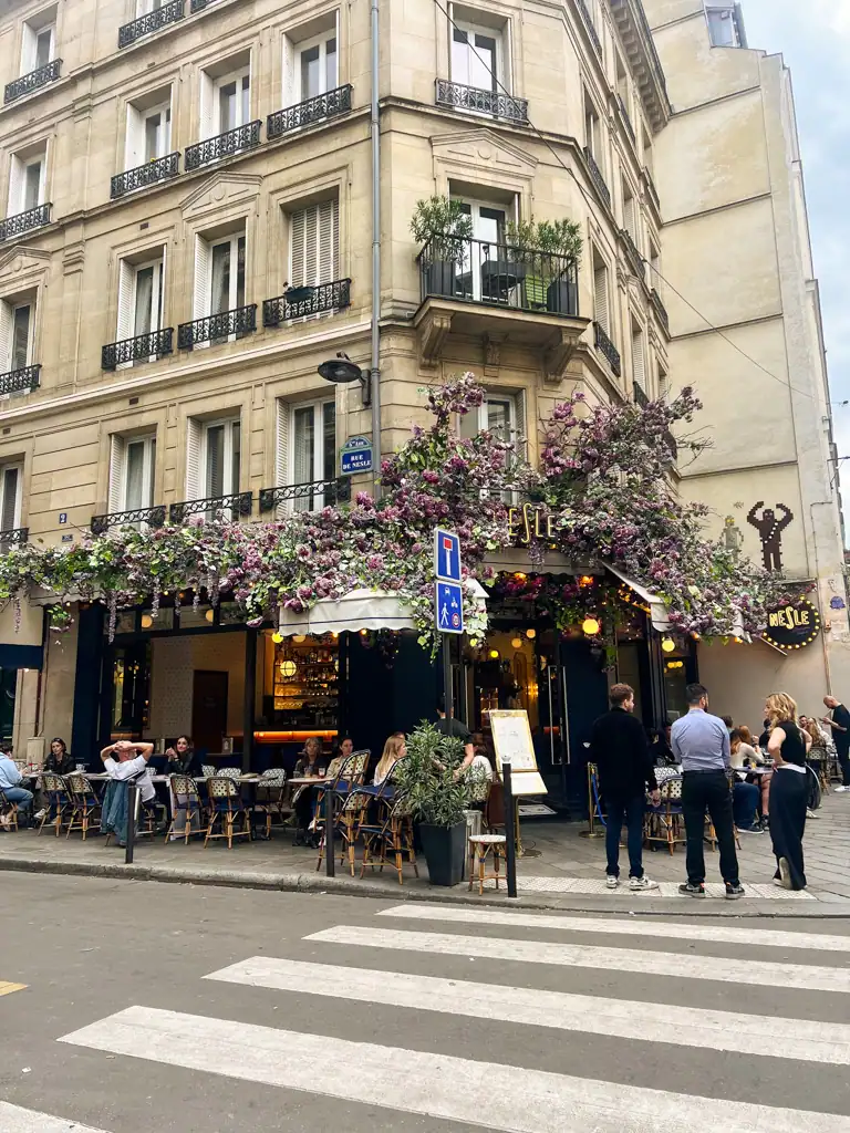 Outside of a typical french bistro with purple flowers surrounding the entrance. 