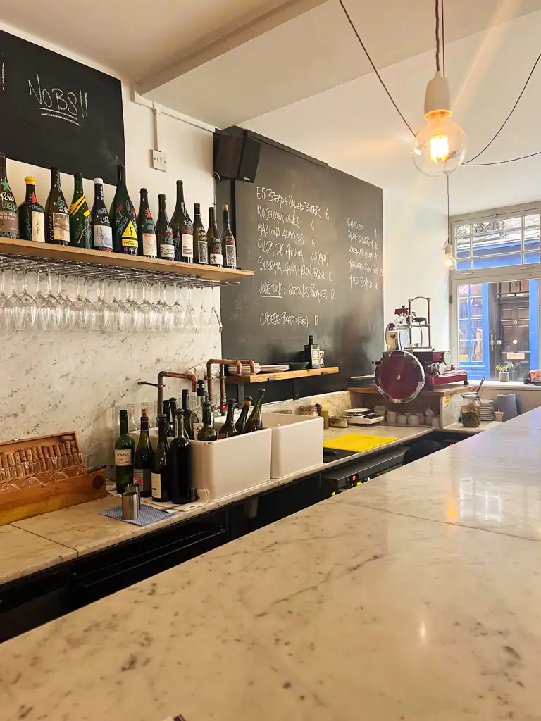 A marble counter top with wine bottles and wine glasses in the background. 