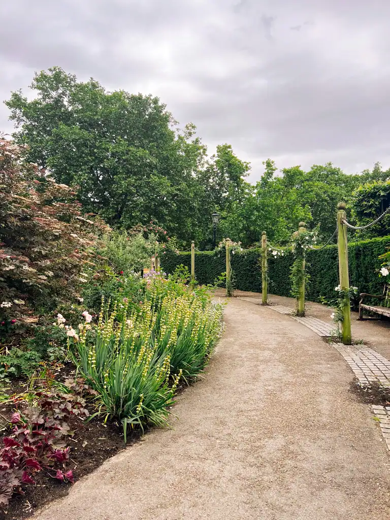 A curved pathway with green bushes, trees and flowers surrounding at Hyde Park. 
