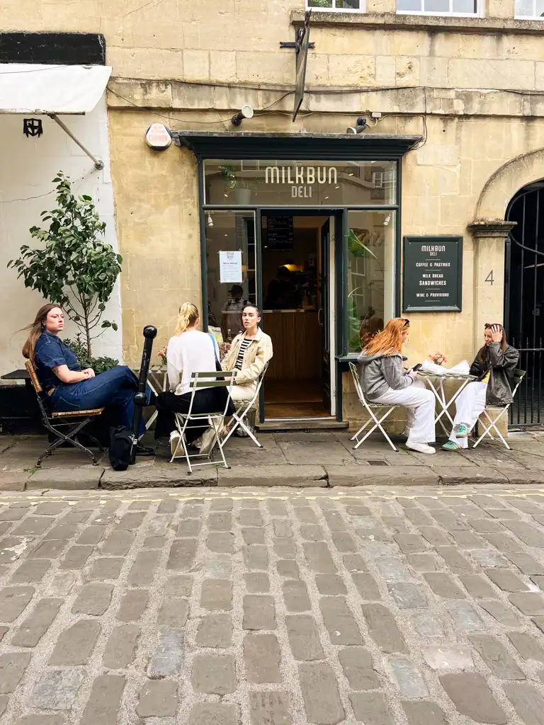The outside of the cafe Milk bun in bath with people sitting on tables and chairs.