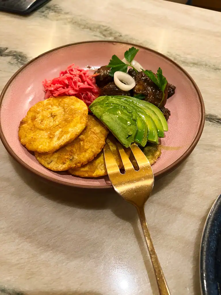 A pink plate with plantains, pork, pickled red onion and avocado at Kann. 