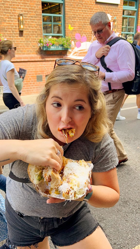 A girl messily eats a large pork sandwich at Borough Market London food guide. 