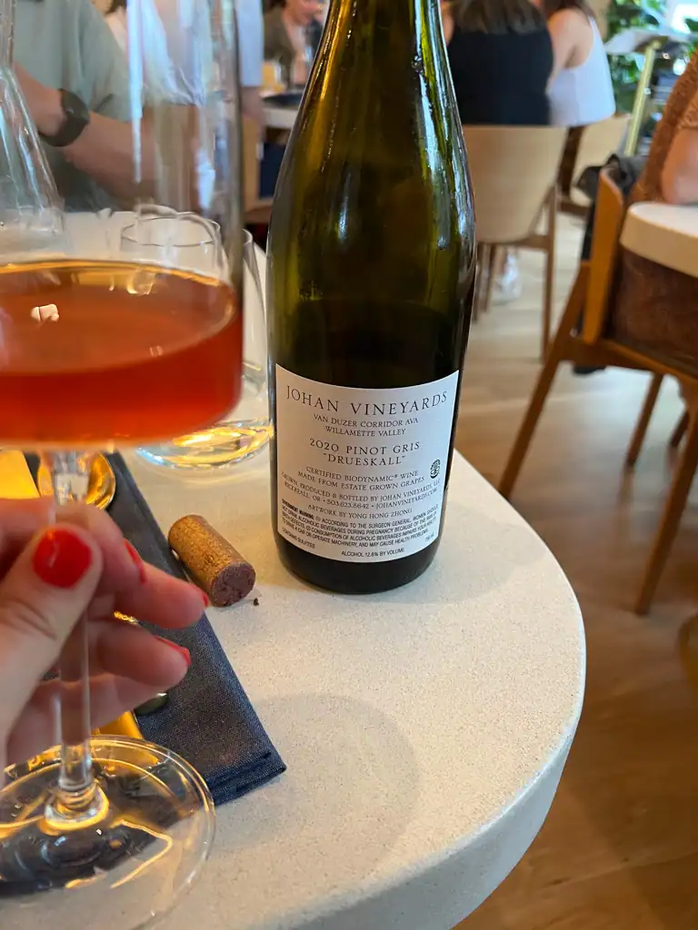 a hand holding a red wine with the bottle in the background at Kann in this Kann review.