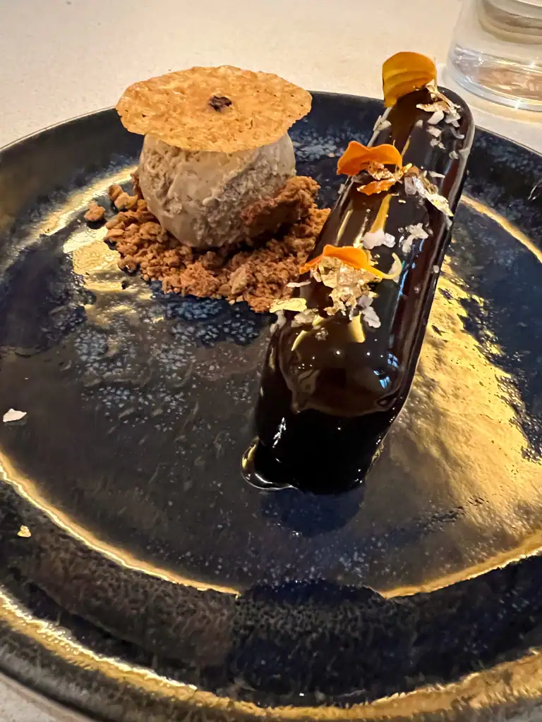 A decadent chocolate eclair dessert with a small scoop of ice cream on a blue plate. 