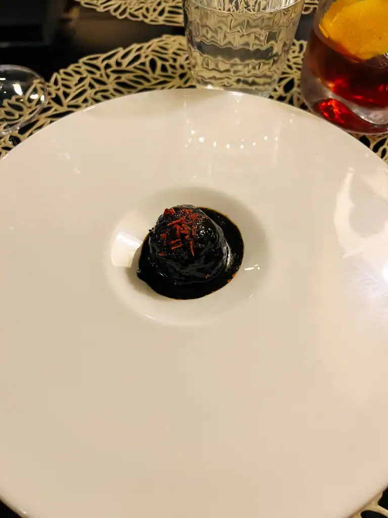Az-zait review of a black food dish with red topping in a very large white plate with a small scooped out middle. 