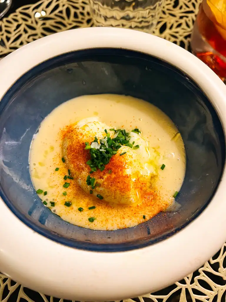 A fish dish in a large white bowl with blue interior in a cream liquid. 