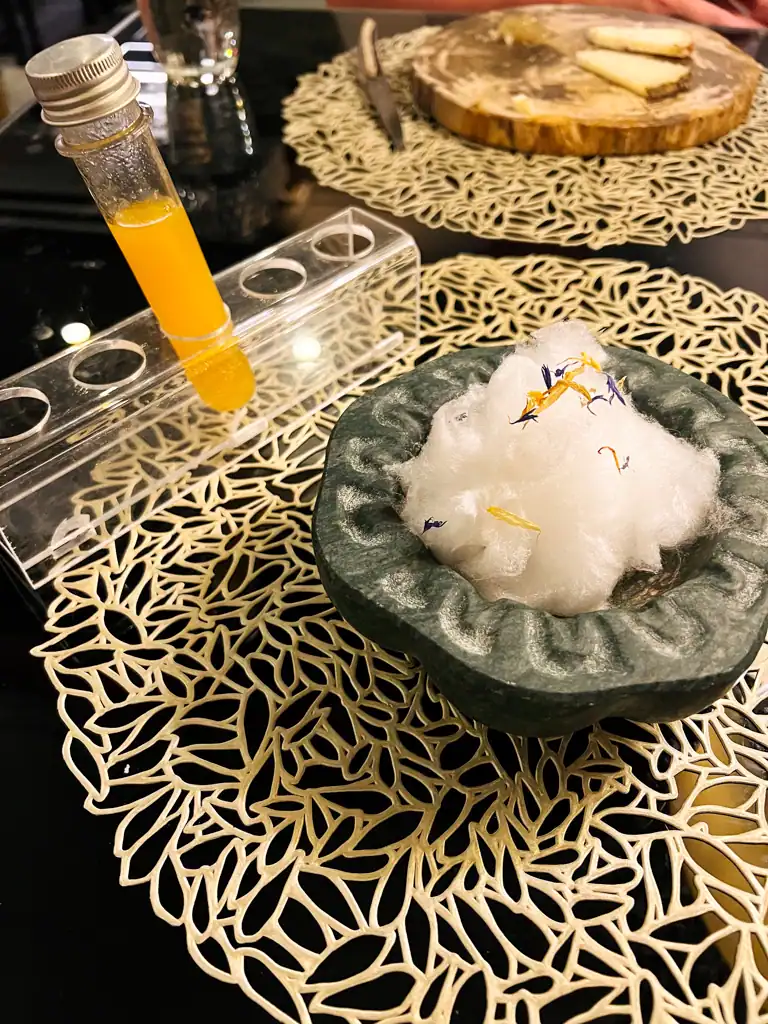 A stone dish with what looks like cotton balls inside and a test tube of yellow liquid to the left. 