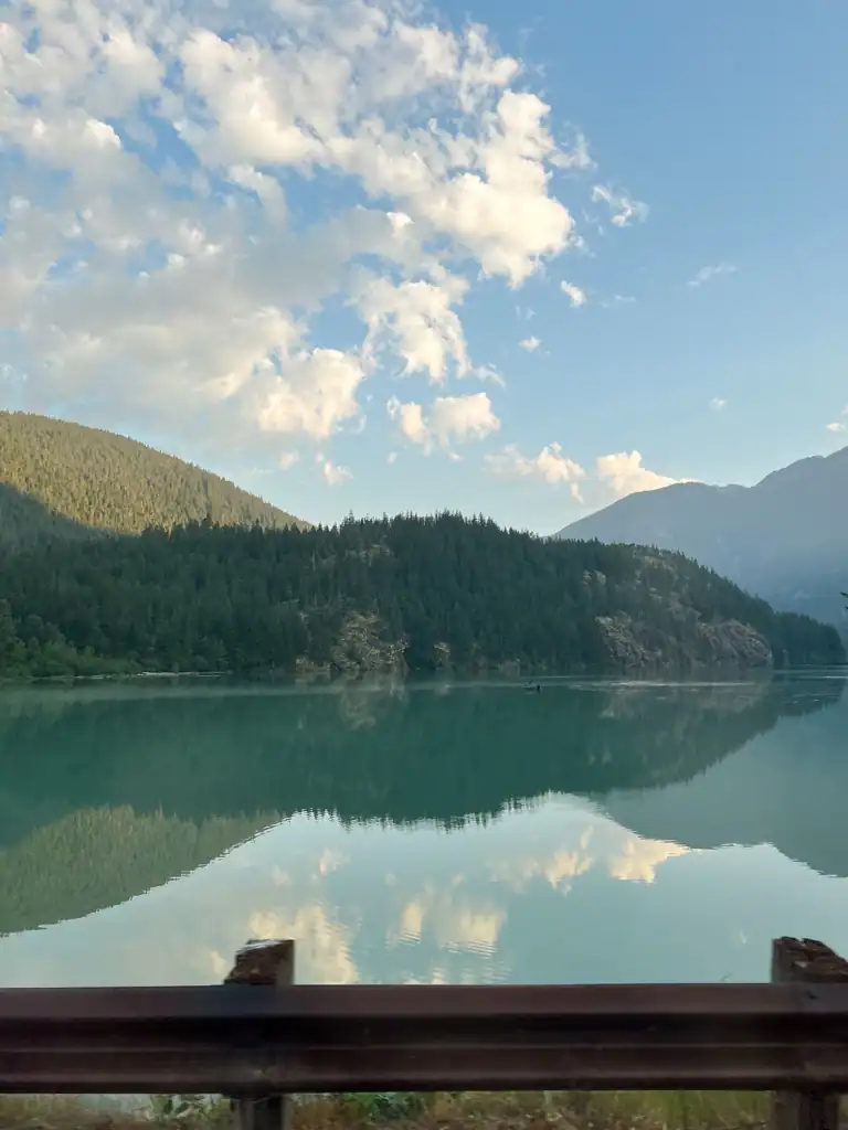 A clear lake reflecting the mountains and clouds during sunrise.