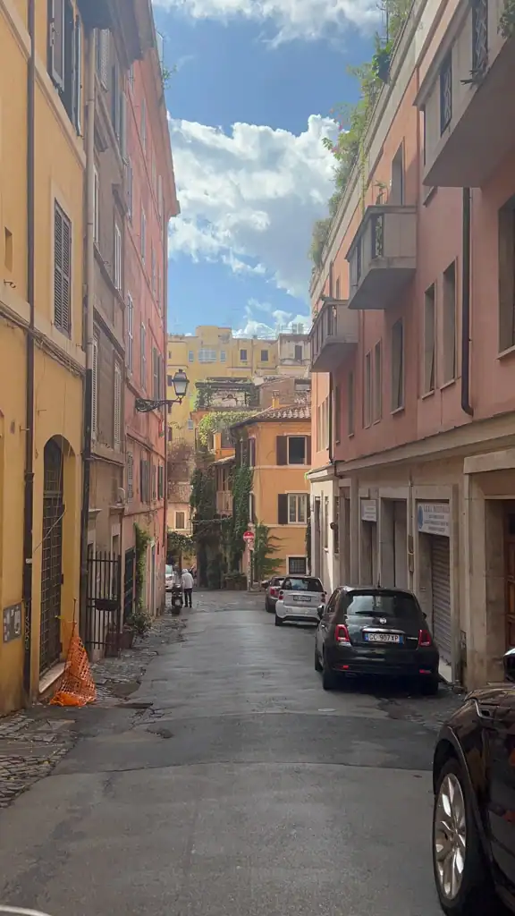 A narrow street in Rome in the Monti neighborhood with pink tinged buildings. 