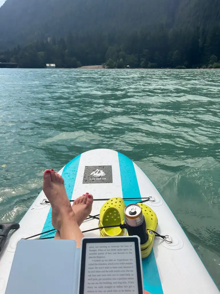 The edge of a stand up paddleboard with yellow crocs on the tip and someone reading a kingle.