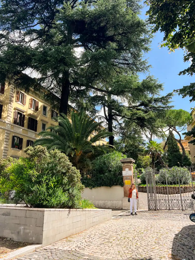 The outside of a park full of trees with a silver gate in the neighborhood of Testaccio. 