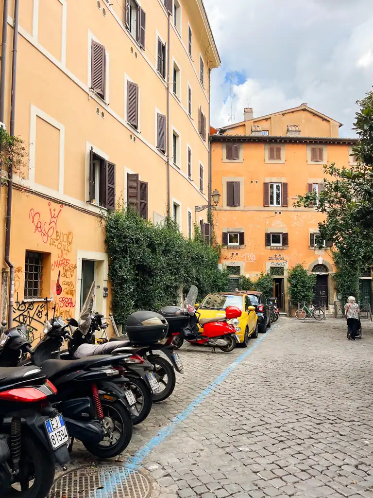 the streets of rome, a woman walking, vespas parked and small yellow cars. 