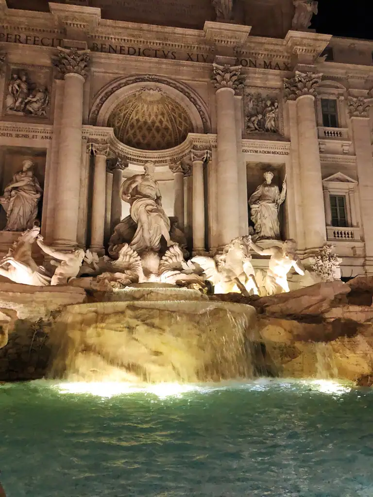 The Trevi Fountain located in the historic center of Rome at night, with the fountain lit up. 