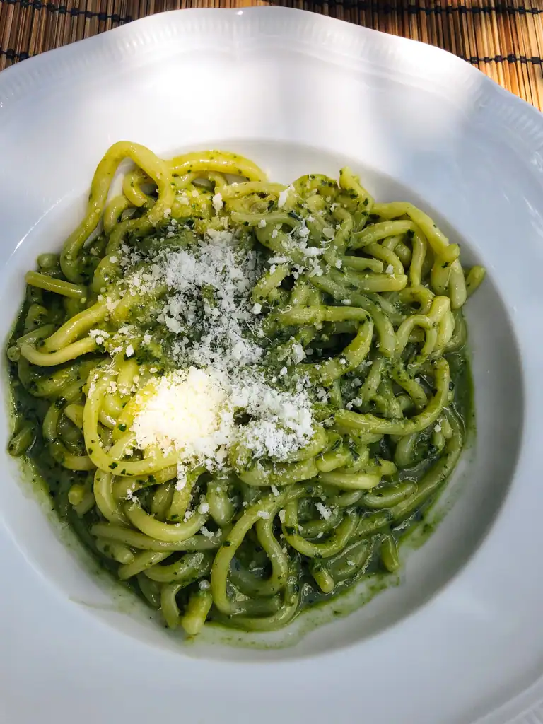 A pesto pasta dish with long noodles and a topping or parmesan cheese in Tuscany. 