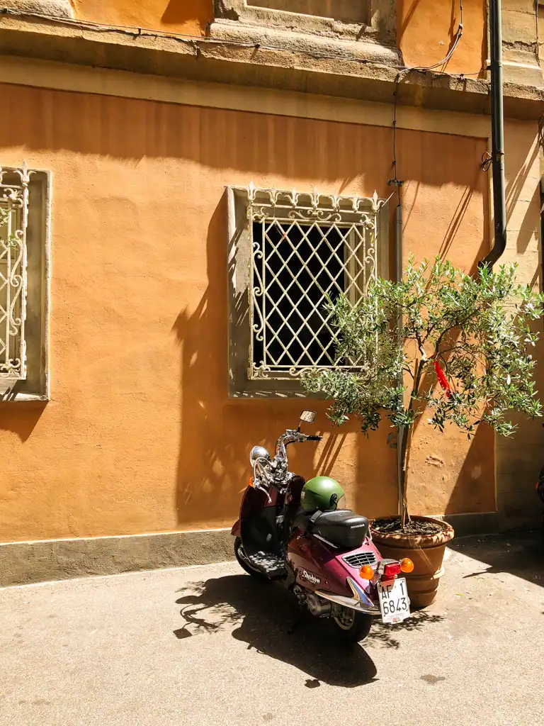A vespa next to an olive tree in Tuscany in one of the 5 towns to visit in tuscany. 
