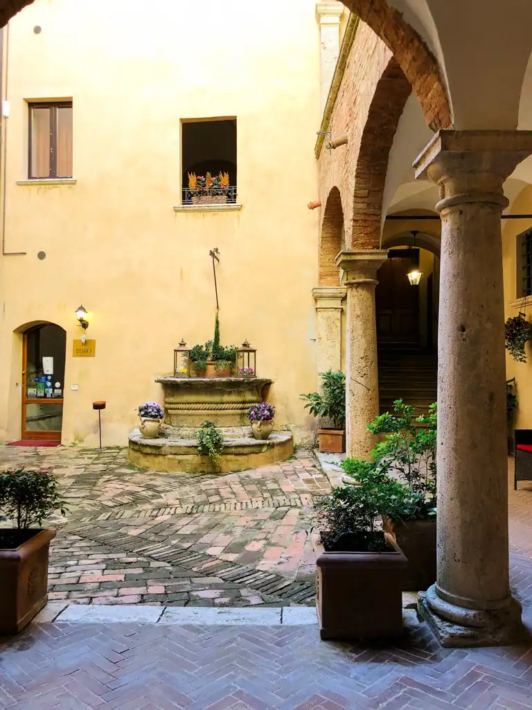 A small courtyard with plants and a small fountain, roman columns and arches in Tuscany. 