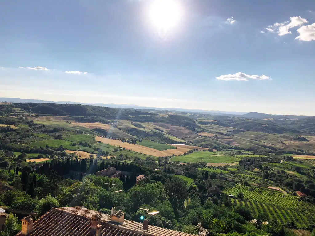A view overlooking the Val d'Orcia which has various colored green and brown fields and vineyards in Tuscany. 