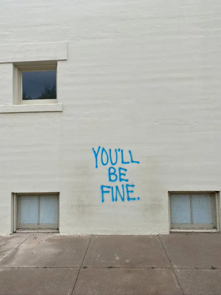 A white cement wall with grafiti that says "you'll be fine". 