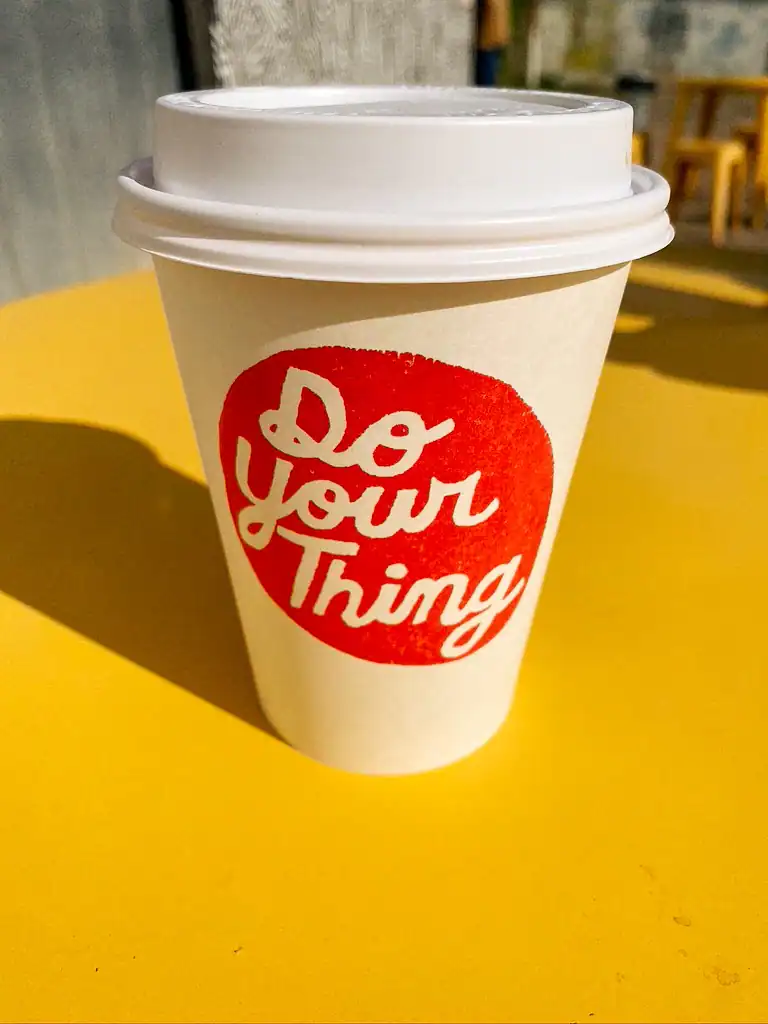A white coffee cup on a yellow table wih a red logo that says "do your thing" in Marfa, Texas. 