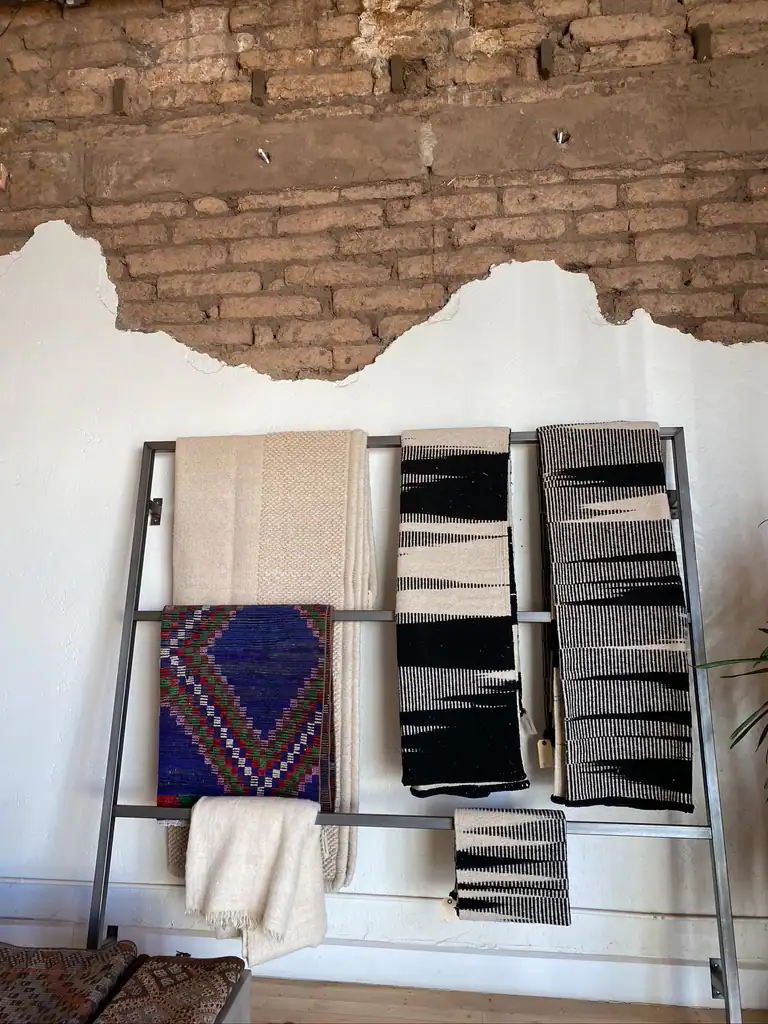 Along the exposed brick walls of teh shop is a blanket hanger with blankets of various sizes and patterns hanging. 