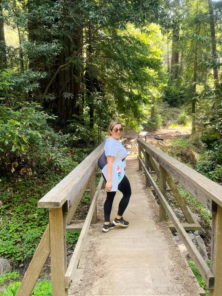 a girl crosses a bridge with wood railings in the forest in this big sur guide. 