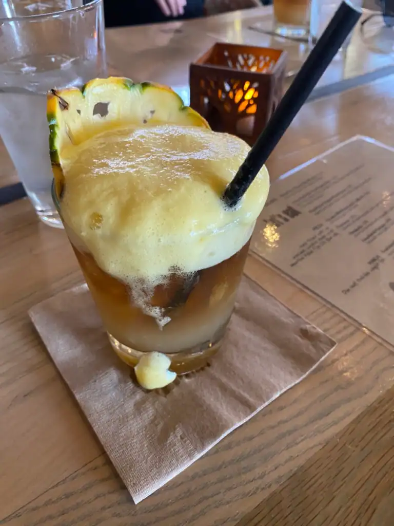 A mai tai with a large black straw and overflowing lilikoi foam. 