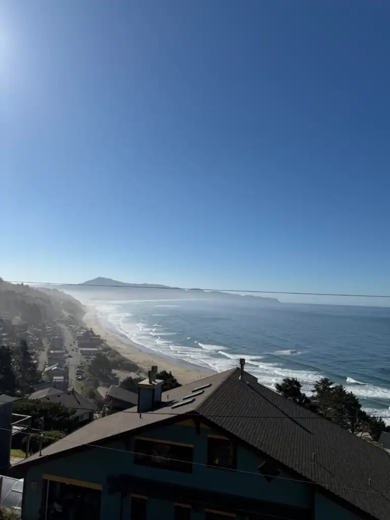 Overlooking a house roofe and the oregon coast, including beach and the surf coming up on the sand. 
