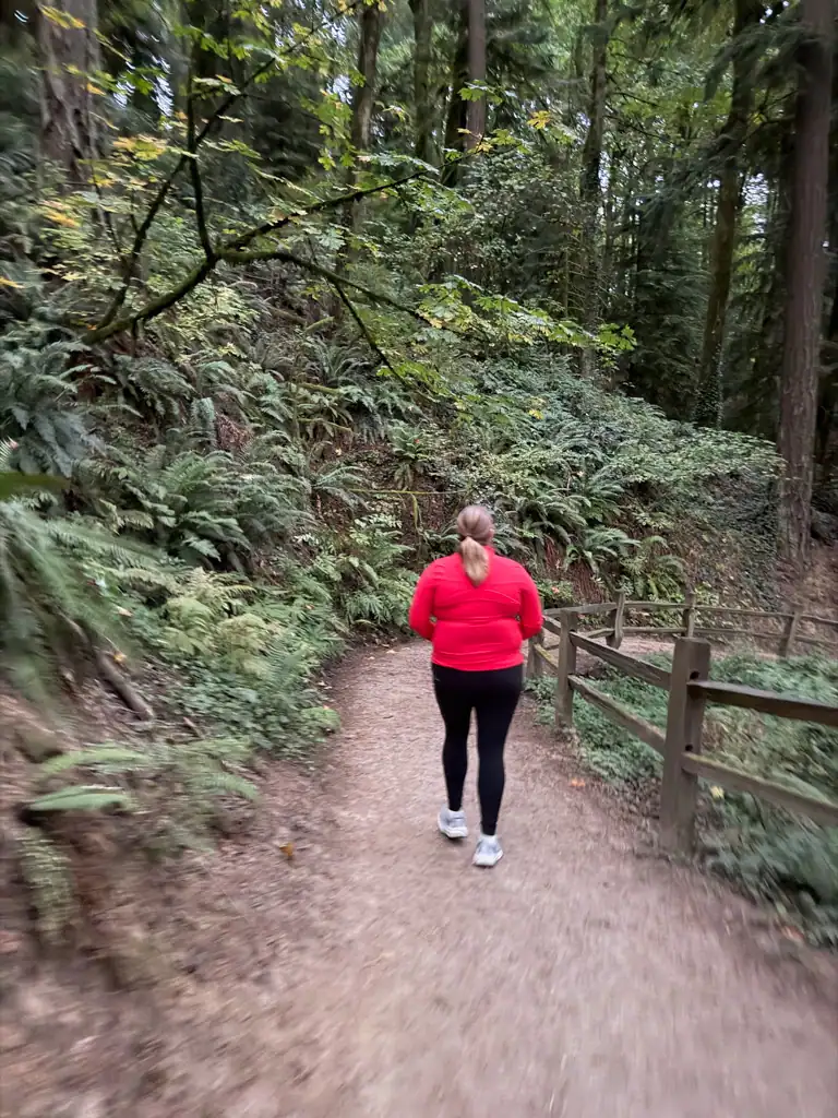 A girl in a red jacket walks the trails with a wooden fence on the right side. 