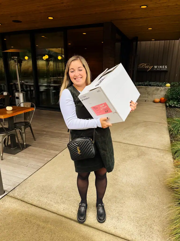A girl holds a large case of wine at a winery, one of the best things to do in Portland. 