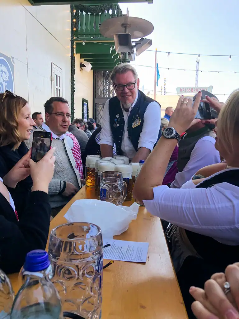 A man with many steins bring them to a table essential oktoberfest guide. 